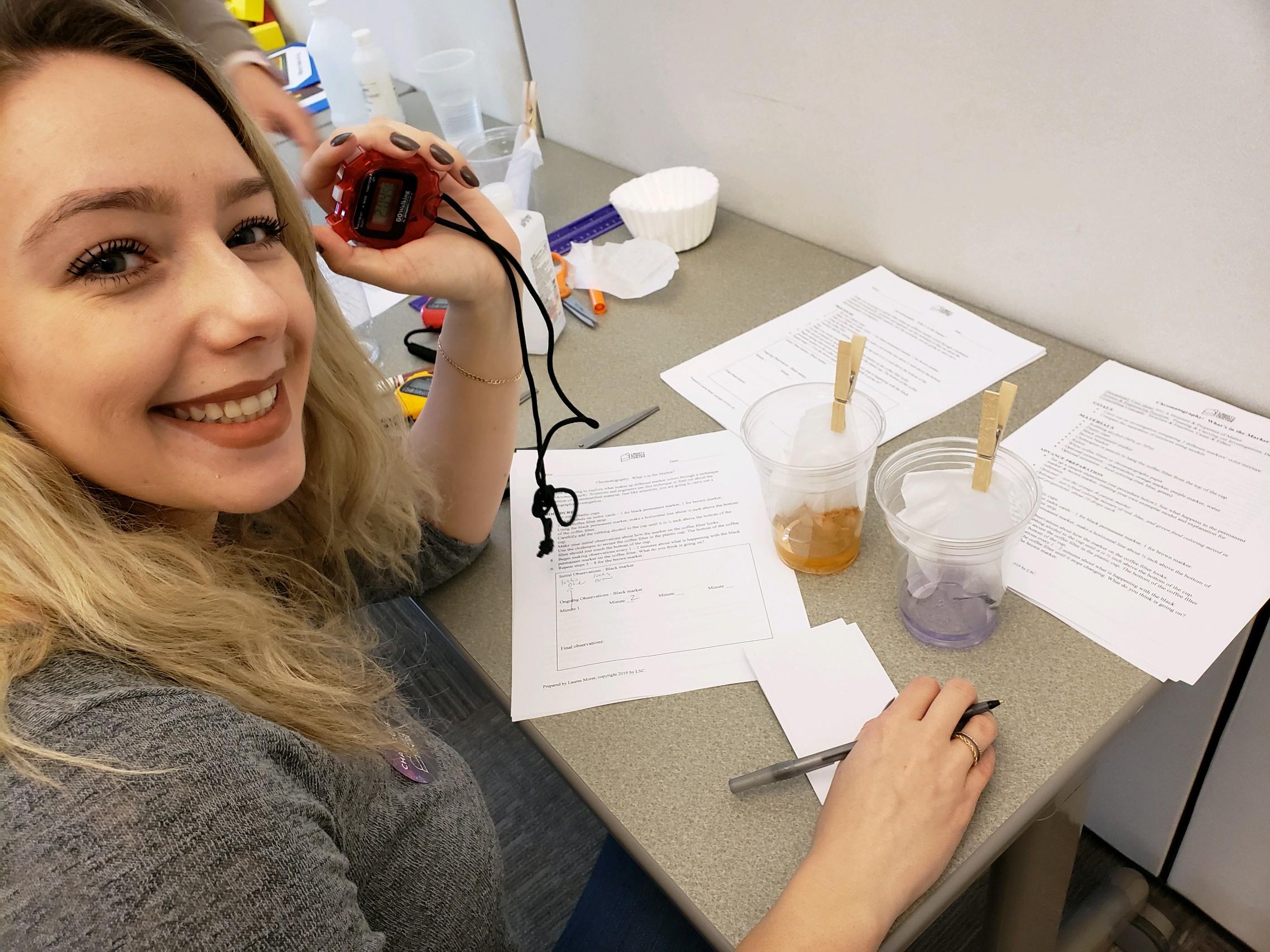 female teacher holding a stop watch to observe two liquids and recording data