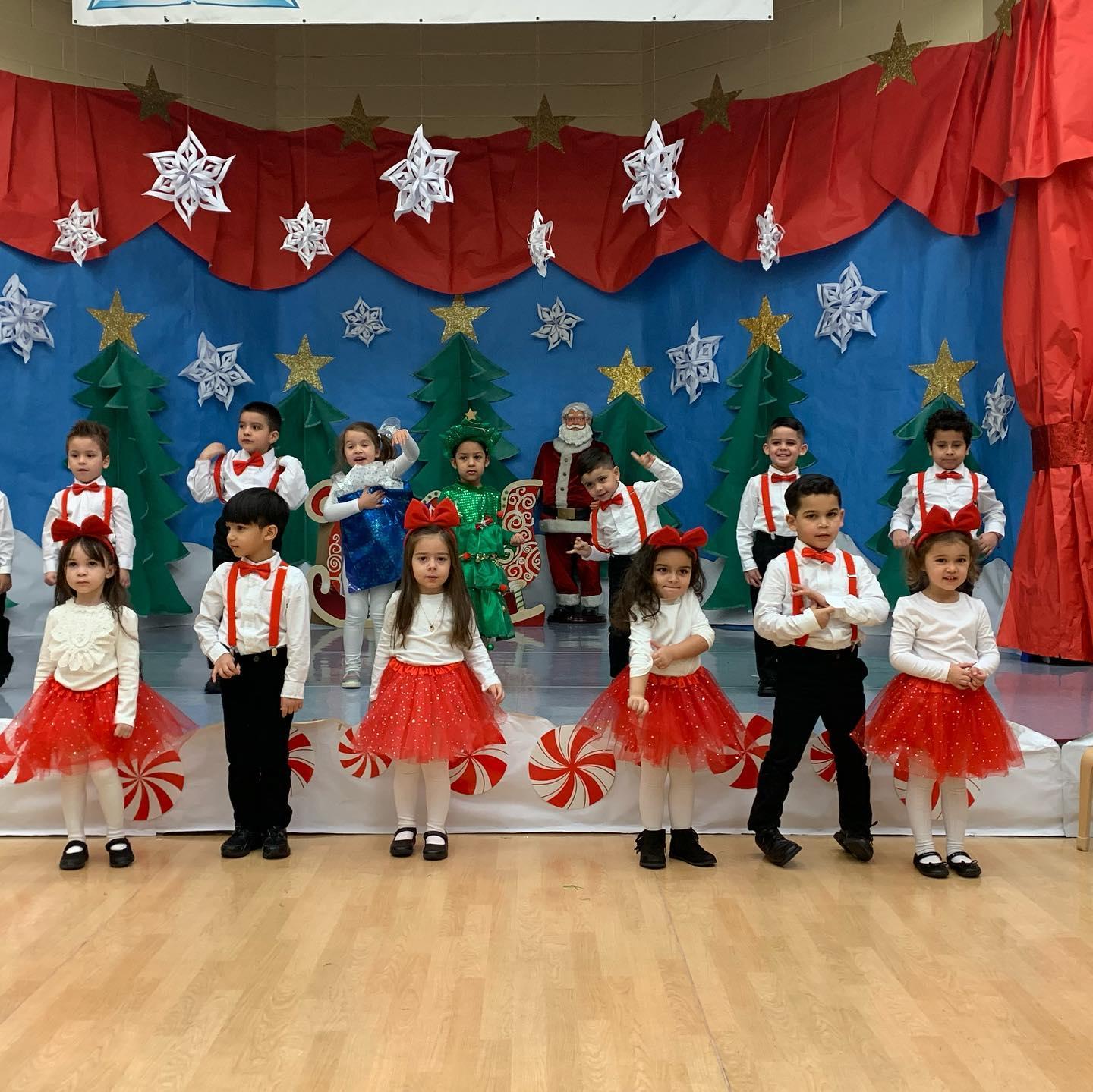 children dressed in white shirts with red skirts and black pant and bow ties on stage