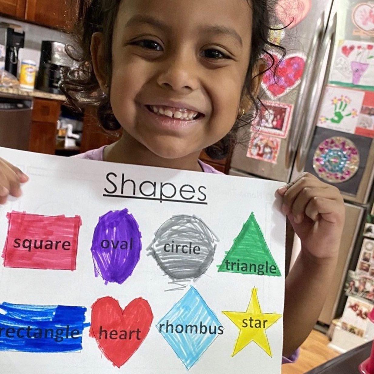 little girl in her kitchen holding up her colored shapes activity